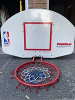 Front of basketball backboard showing NBA and Huffy Sports logos with red square target and red rim with net attached.