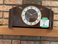 Front view of Blackforest wooden mantel clock on shelf, showing round white face with black numerals and hands under glass, fluted wood side columns.