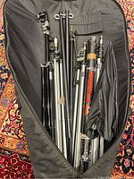 Top angle view of collection of studio light stands and umbrellas inside black carrying bag on patterned carpet.