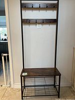 Front view of dark wood and metal coat rack with bench and hooks.