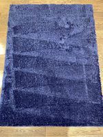 Full top-down view of dark blue shag carpet on hardwood floor showing solid color and texture.