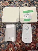 Photo of all four networking devices showing two Apple AirPort Extreme Base Stations, a Eufy HomeBase 2, and a TP-Link Wi-Fi Range Extender on a patterned carpet.