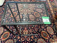 Glass top rectangular table with black metal frame and C-shaped base photographed against patterned carpet.