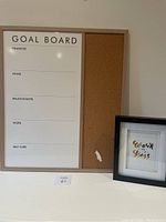 Goal board with whiteboard and cork board sections shown with visible writing areas and small hole in cork board section. Adjacent framed gold embossed print with 'Work Like a Boss' text visible.