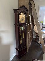 Full view of the tall wooden grandfather clock next to a bookshelf, showing overall size and style.