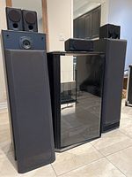 Full view of large Kenwood speakers, smaller satellite speakers on top, and black glass-front cabinet.