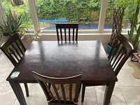 Dark wood rectangular kitchen table with four matching chairs around it, chair backs visible.