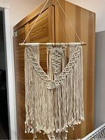 Front view of the macrame wall hanging showing intricate knot patterns and gold bead accents with long fringe