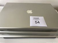 Stack of 3 silver Apple MacBook laptops showing closed lids with Apple logo on top laptop