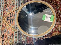 Photo of the round mirror face up on a patterned carpet, showing the grey frame wrapped in natural jute rope with a hanging loop.