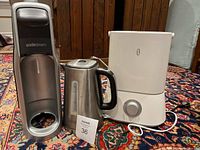 Photo showing the SodaStream carbonator machine, a stainless steel electric kettle, and a white humidifier on a patterned rug.