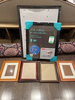 Six picture frames arranged side by side on floor including two large black IKEA SASNÄS and various smaller wood frames
