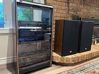 Wide shot of the audio system cabinet with glass doors and a pair of speakers beside it on the floor.