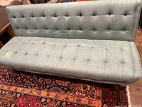 Front view of turquoise sofa in upright position showing tufted cushioning and leg style