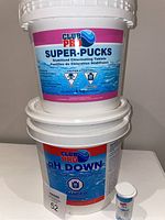 Photo of three containers: Club Pro Super-Pucks bucket, Club Pro PH Down bucket, and HTH spa test strips container