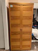 Closed wardrobe showing two doors with vertical slat design and round wooden handles.