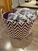 Photo of purple and white chevron patterned fabric bin containing gray blanket.