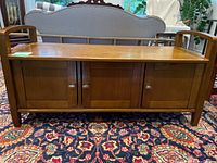 Front view of wooden bench with three storage doors and seating top on patterned rug.
