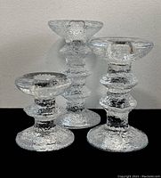 Three clear glass Iittala candle sticks with textured glass design, varying heights, on black and grey backgrounds. Shows overall shape, size, and condition.
