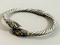 Full view of the twisted silver bangle showing double dragon heads with yellow eyes and decorative band detail.