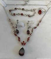 Photo shows full set of garnet-colored costume jewelry on white display, including necklace, earrings, bracelet, and ring.