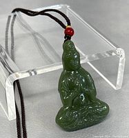 Front view of the green jade Guanyin pendant on a brown cord showcased against a grey background and clear display stand.