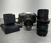 Frontal view of Konica Autoreflex T3 camera with 50mm lens mounted, additional lenses to the right, flash unit on the left.