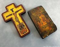 Photo showing the wooden crucifix with Jesus Christ and rectangular plaque with religious scene placed together on a flat surface.