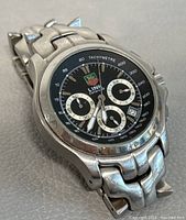 Angled front view showing black dial, silver sub-dials, integrated S-link bracelet