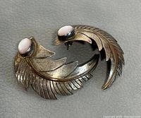 Pair of vintage 925 sterling silver earrings with pink cabochon stones shown side by side. Curved feather design visible with detailed feather engraving.