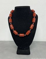 Front view of the red coral necklace displayed on a black bust showing large cylindrical coral beads and smaller spacer beads.