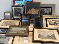 Group of antique framed prints and photos on a table, showing cityscape prints, vintage photo, and artistic print with various frames