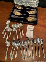 Four ornate shell bowl spoons in velvet-lined case with four matching silverplated teaspoons laid out on wood table