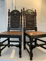 Front view of the pair of dark carved wooden chairs with detailed backs and twisted spindle legs.