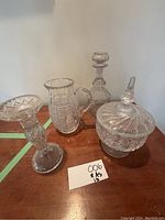 All four items displayed on a wooden surface: candle holder, pitcher, decanter, candy bowl with lid.