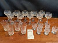 Full lot showing 18 glassware pieces arranged on table with a variety of stemmed glasses, highball glasses and small glasses with hexagonal bases.