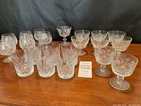 Photo showing full assortment of twenty assorted crystal glasses arranged on a wooden surface.