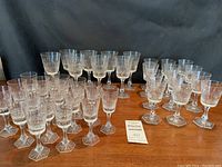Full set of 40 crystal stemware glasses displayed on wooden table, arranged in groups by size. Hexagonal bases visible.