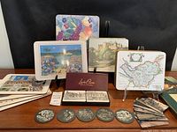 View of various coasters and placemats arranged on a wooden table showing multiple designs including a boxed coaster set and various maps and scenic prints.