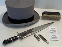 Overview of the gray London top hat, large decorative Bowie-style knife, two small pocket knives, and a lint brush with hidden compartment