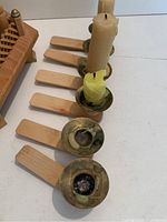 Close-up of six detached wooden candle holders with brass cups, some containing melted wax residue.