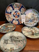 Group photo of the five hand-painted porcelain plates with various detailed Asian-themed artwork including figures, architecture, and floral decorations.