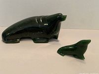 Two dark green jade seal figurines photographed side by side on a plain light surface, showing size difference and shape details.