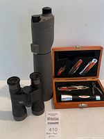 Full lot view including binoculars, scope, and wooden box with multi-tools and flashlight.