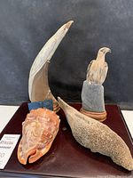 Four natural art carved figures displayed on a flat surface: two birds, a seal, and a carved shell with mermaid relief.