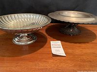 Two pedestal servers side by side: fluted lobed bowl with beaded rim on pedestal base at left; scalloped-edge compote on pedestal at right