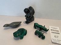 Group photo showing all five animal figurines on a white surface: four green malachite animals (two rhinoceroses, frog, hippopotamus) and one black soapstone bird.
