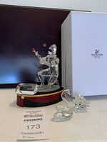 Photo of all three figurines including the Harlequin on display base, swan, and hedgehog with original Swarovski box in background.