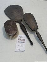 Three-piece vanity set: handheld mirror, hair brush, and lint brush showing overall condition and tarnish.