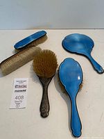 Full view of all five items displayed on white background - two lint brushes, handheld mirror, two hair brushes with natural bristles.